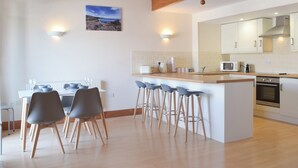 Eine moderne Küche mit weißen Schränken, einer Holztischinsel mit Barhocker und einem Essbereich mit Tisch und Stühlen.