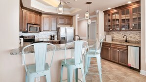 A modern kitchen with wooden cabinets, a stainless steel refrigerator, and a granite countertop. - The Oasis 409 | Spacious, Lazy River, Poolside Grill, New Splash Pad, Pool with Slide! (Orange Beach)