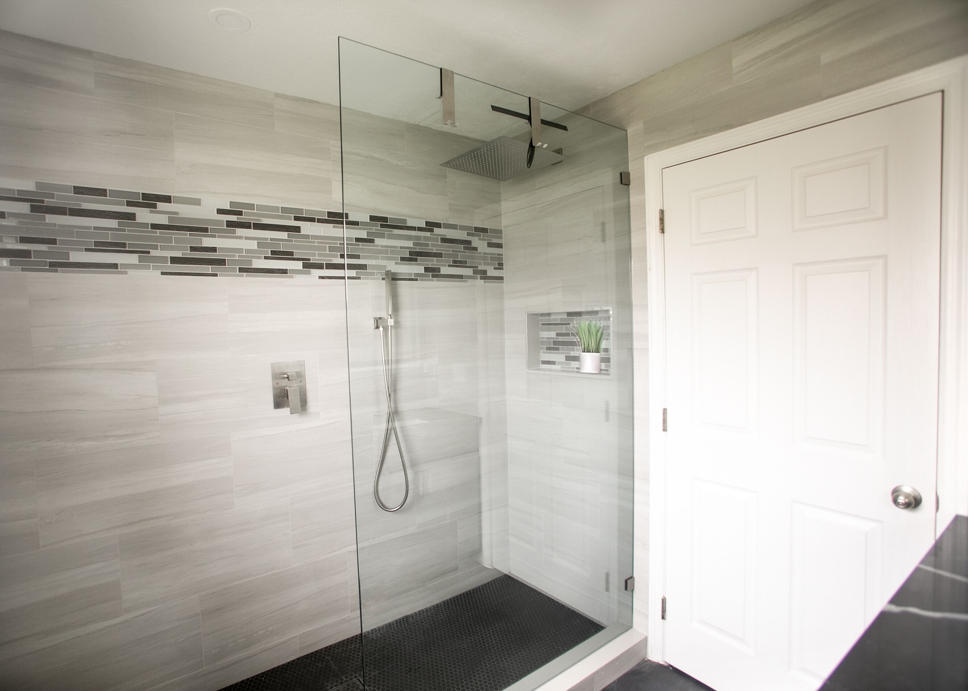 Une salle de bain moderne avec une douche à parois de verre, un mur recouvert de carreaux et une porte blanche.