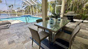 A covered outdoor area with a pool, dining table, chairs, and a grill. - Contemporary waterfront pool home with Gulf access (CAPE CORAL)