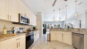 A modern kitchen with white cabinetry, a stainless steel range, and a marble countertop. - Contemporary waterfront pool home with Gulf access (CAPE CORAL)