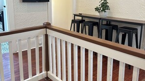 Una escalera con barandales blancos y un pasamanos de madera, que conduce a un comedor con una mesa y sillas.