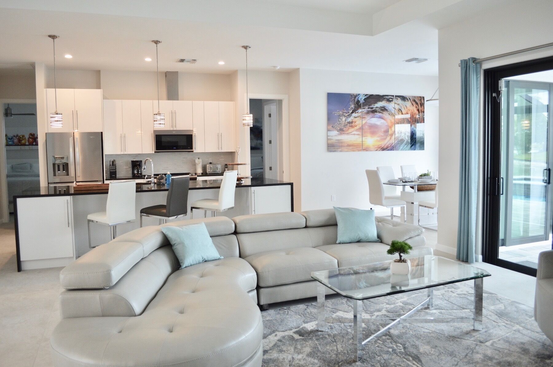 A modern living room with a large L-shaped sectional sofa, a glass coffee table, and a dining area with a white table and chairs.