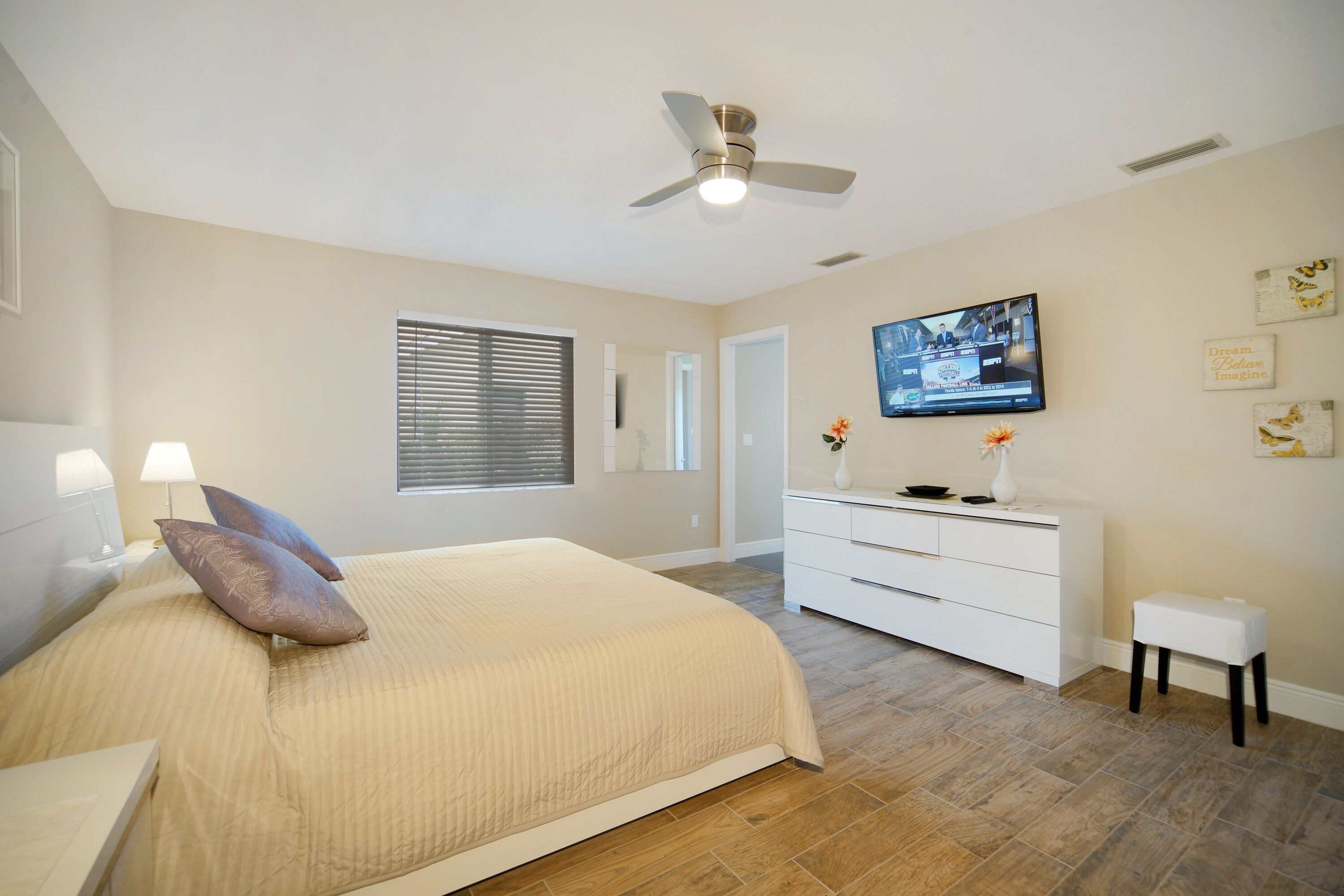 Un dormitorio con cama, cómoda, televisor y ventilador de techo.