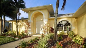 A residential building with a yellow facade, a central arched entrance, and a large window with a grid design. - Waterfront home with a Billiard table pool and spa (CAPE CORAL)