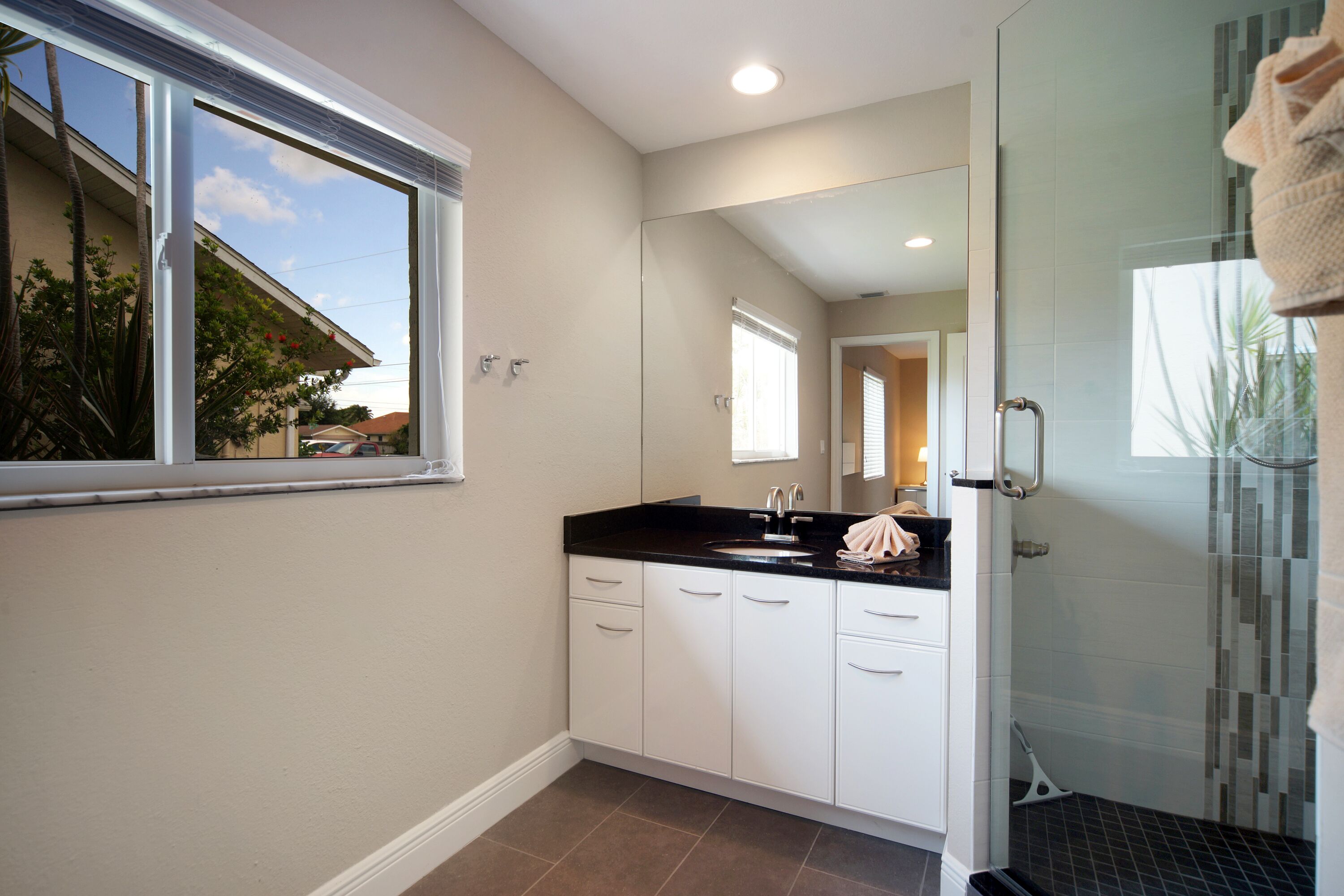 A modern bathroom with a large window, a shower with a glass door, and a sink with a black countertop.