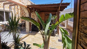 Un edificio de paredes de piedra con una pérgola de madera y grandes plantas verdes.