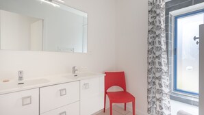 Une salle de bain avec un meuble-lavabo blanc, une chaise rouge, un grand miroir et une fenêtre ornée d’un rideau à motifs de papillons.