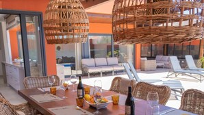 A dining area with wicker furniture, a wooden table set for a meal, and a poolside view. - Villa Privada de Lujo con Piscina, Villa Sabi Sabi (Corralejo Playa)