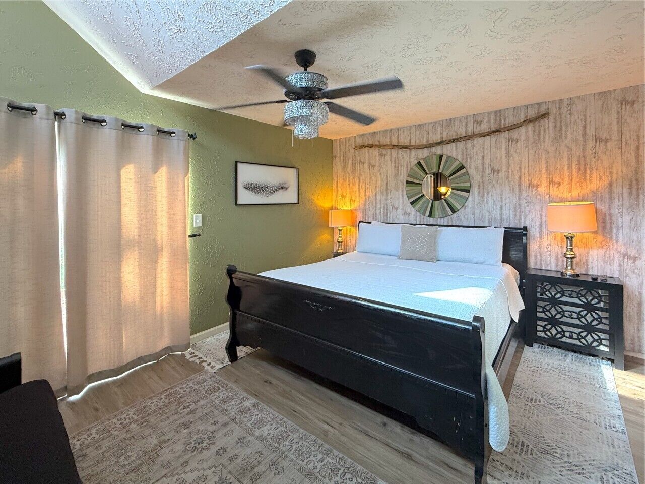 A bedroom with a bed, a ceiling fan, a wall clock, and two bedside lamps.