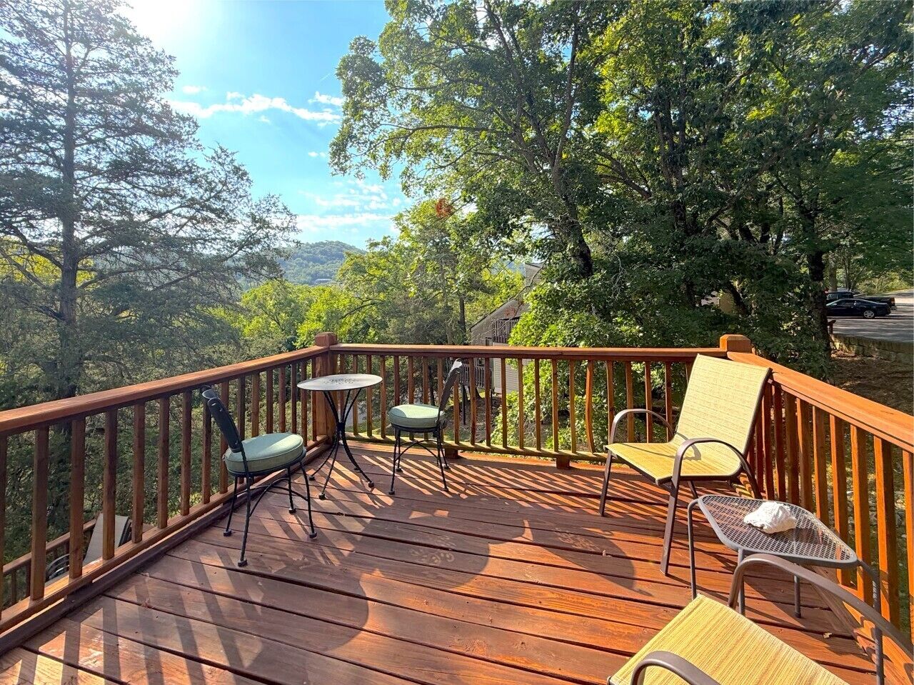 Una terraza de madera con barandilla, rodeada de árboles y cielo despejado.
