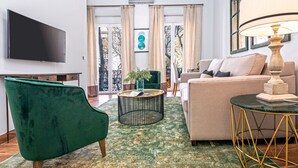 Un soggiorno con una TV a schermo piatto, una poltrona verde, un divano beige, un tavolino rotondo e una lampada.