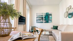 Un salon avec une table en bois, un fauteuil vert, un canapé beige et des œuvres d’art abstraites accrochées au mur.