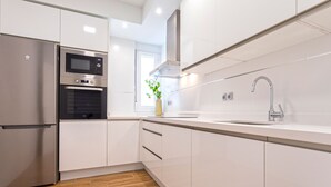 Une cuisine moderne avec des meubles blancs, un réfrigérateur en acier inoxydable, un four encastré, un four à micro-ondes et un évier doté d’un robinet contemporain.