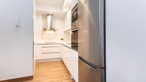 Une cuisine moderne avec des armoires blanches, un réfrigérateur en acier inoxydable et un four encastré.