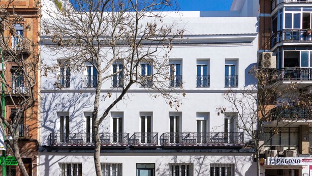 Un bâtiment blanc avec de nombreuses fenêtres et des balcons, une porte verte et, sur la droite, un café appelé « Palomo ».
