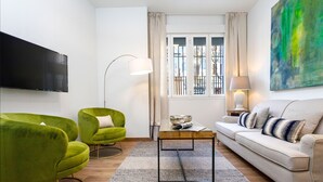 En moderne stue med et fladskærms-tv, to grønne lænestole, en beige sofa og et sofabord.