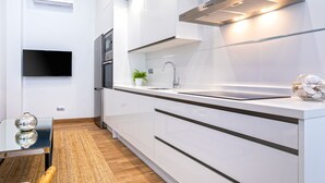 Een moderne keuken met witte kasten, een roestvrijstalen afzuigkap, een inbouwoven en een flatscreen televisie aan de muur.