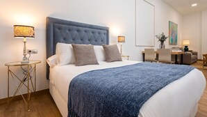 Een slaapkamer met een groot bed, twee nachtkastjes met lampen, een bureau met stoelen en een schilderij aan de muur.