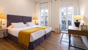 Une chambre d’hôtel dotée d’un grand lit, de deux tables de chevet avec des lampes, d’un bureau avec une chaise et offrant une vue sur l’extérieur grâce à de grandes fenêtres.