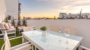 Une terrasse sur le toit avec une table blanche dressée pour le dîner, entourée de chaises blanches, et une petite plante en pot.