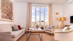 Un salon moderne avec un canapé, des fauteuils, une table basse et une grande fenêtre avec des rideaux.
