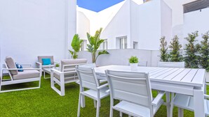 Un patio exterior blanco con una mesa y sillas, rodeado de muros blancos y césped verde.