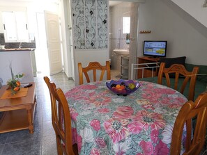 A dining area with a floral tablecloth, wooden chairs, and a fruit bowl.