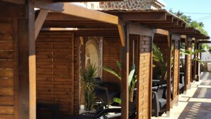 A row of wooden structures with outdoor seating, a stone wall, and potted plants. - Terraced apartment André A3 by the sea (Els Poblets, Comunidad Valenciana)