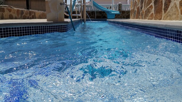 A swimming pool with a slide, stone walls, and a clear sky. - Terraced apartment André A3 by the sea (Els Poblets, Comunidad Valenciana)