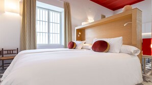 Ein Hotelzimmer mit einem großen Bett, zwei Kissen, einem Holzkopfteil, einer Bank und einem Fenster mit Vorhängen.