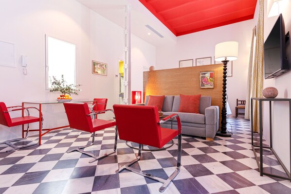 Una sala de estar moderna con suelo de cuadros, sillas rojas, un sofá gris y un cabecero de madera.