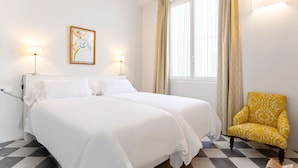 Een hotelkamer met een groot bed, twee bedlampen, een ingelijste afbeelding, een raam met gordijnen en een gestreept fauteuil.