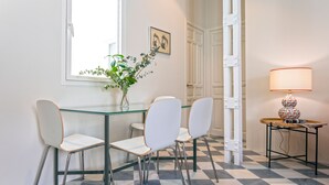 A dining area with a glass table, white chairs, a vase with greenery, a lamp, and a checkered floor. - Genteel Home San Laureano VI (Seville)