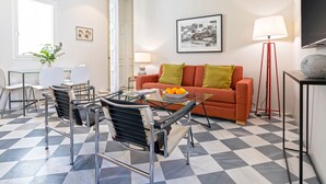 A modern living room with a checkered floor, a glass coffee table, a sofa with cushions, a side table, a lamp, and a framed picture on the wall. - Genteel Home San Laureano VI (Seville)