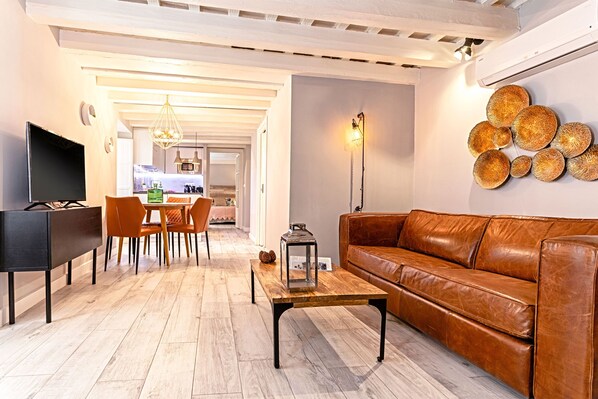 A living room with a brown leather sofa, a wooden coffee table, a TV, and a dining area with chairs and a table. - Genteel Home Plaza de España II (Cadiz)