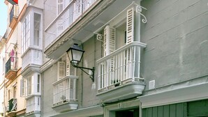 Eine Reihe historischer Gebäude mit weißen Balkonen und grünen Fensterläden, dazu eine gepflasterte Straße.