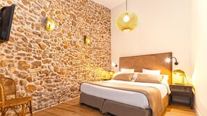 Ein Schlafzimmer mit einer Steinsäule, einem Bett mit hölzernem Kopfteil, einem Korbstuhl und Nachttischlampen.