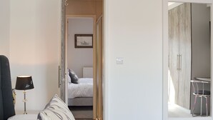 A hotel room with a bed, a bedside lamp, a chair, and a view of the hallway.