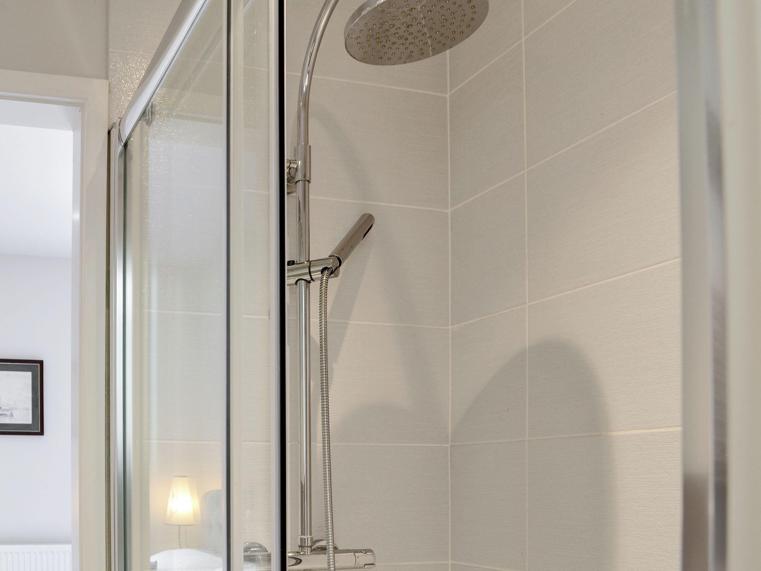 Une douche fermée par des parois en verre, dotée d’un pommeau de douche à main et d’une douchette à pluie fixée au mur.