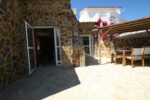A stone building with an open door leading to a covered patio area with a table and chairs.