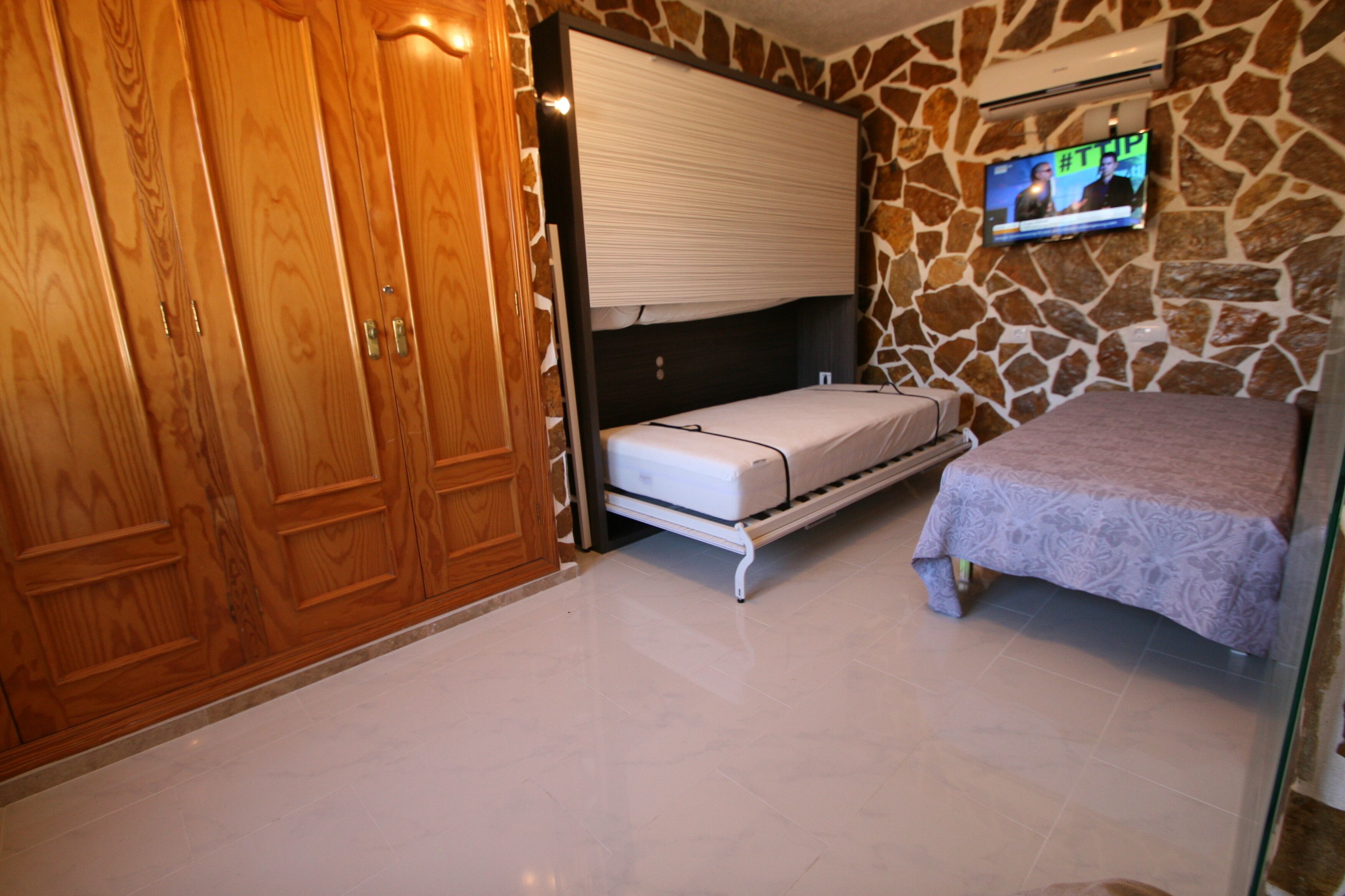 A bedroom with a bed, a TV mounted on the wall, and a wardrobe.