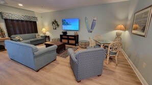 A living room with a sofa, armchair, coffee table, TV, and dining area with chairs and a lamp.