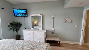 A bedroom with a bed, dresser, TV, potted plant, and a captain's wheel decoration.