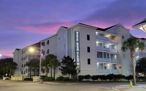 A multi-story hotel with a prominent vertical sign, balconies, and a street view. - MBV 6Br - Palm Breeze (Myrtle Beach)