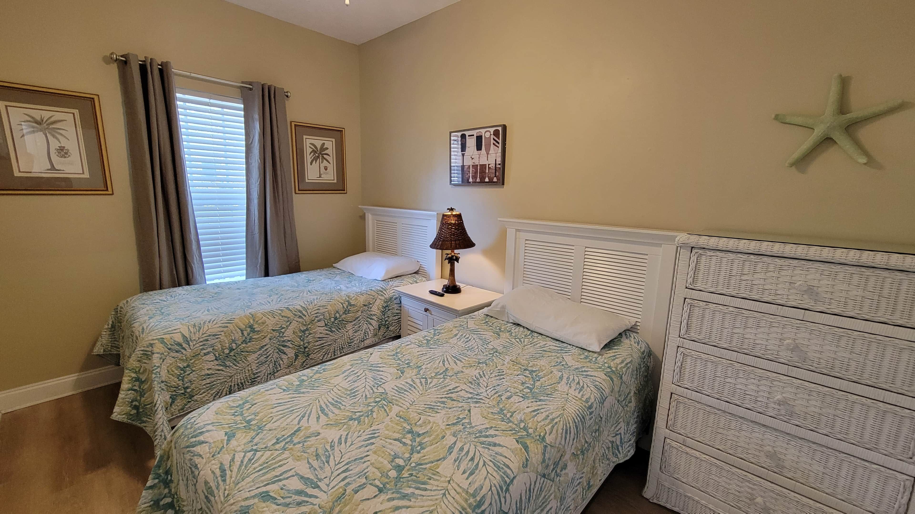 A bedroom with two beds, a nightstand with a lamp, a starfish decoration, and two framed pictures on the wall.