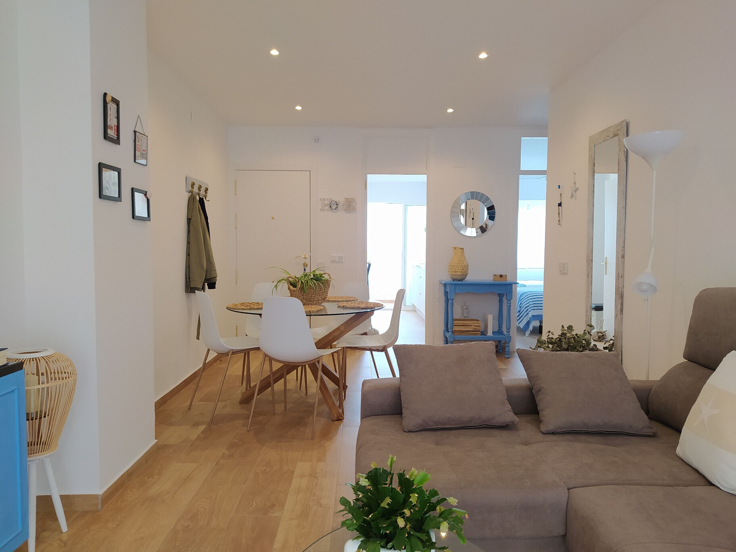 A modern living room with a sofa, a dining area with a glass table, and a blue console table.
