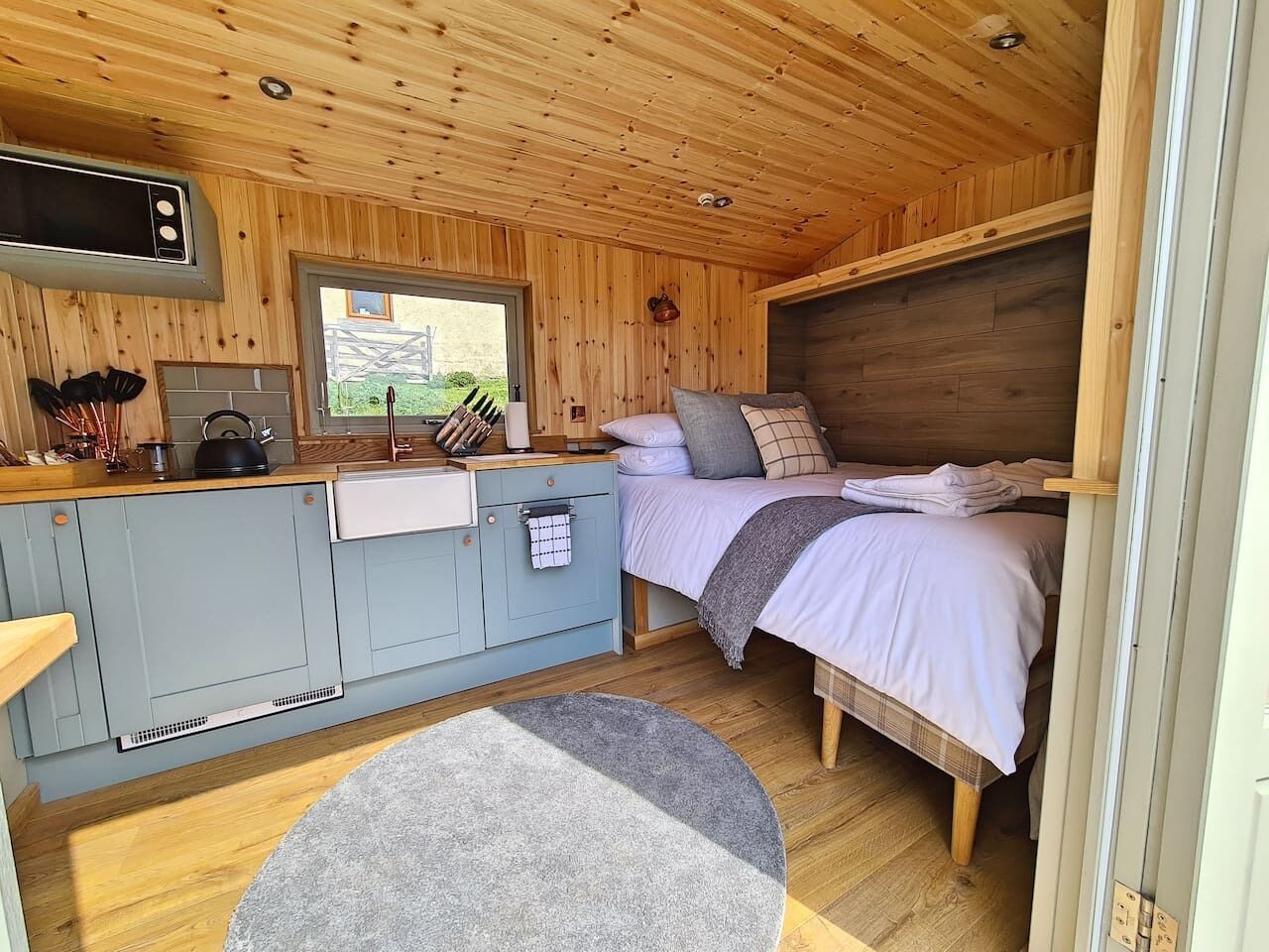 A compact cabin-style room with a kitchenette, a bed with a headboard, and a small round rug.