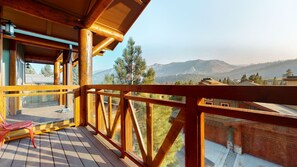 A wooden balcony with a view of mountains and pine trees.