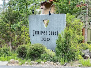 Situated in a residential neighborhood, Juniper Crest 100 features a well-maintained garden with lush greenery and a stone sign.